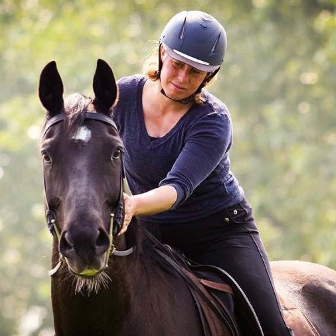 Astrid te paard op een donker paard in het bos